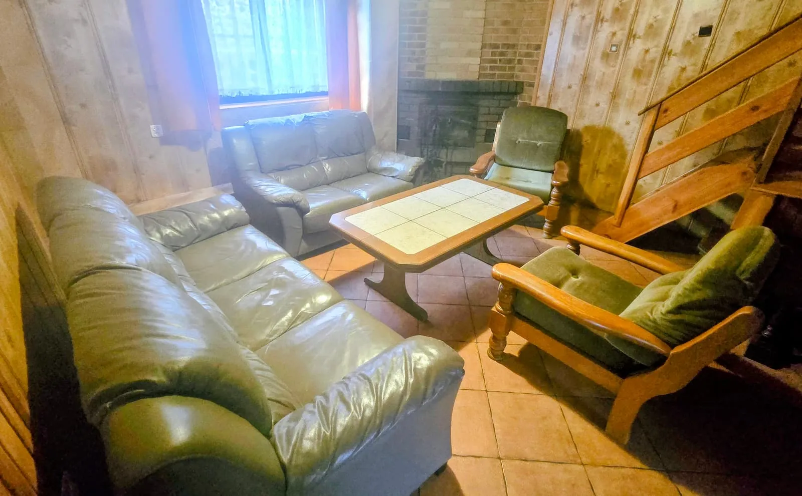 Domek 2 w ośrodku Ambrowil w Lidzbarku Welskim – salon z sofą, stolikiem i drewnianymi schodami